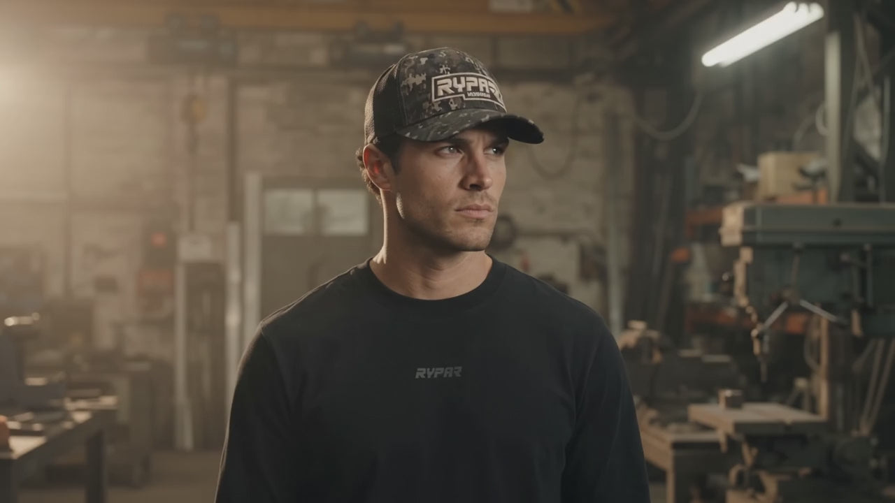 Man wearing a RYPA camo trucker cap and black RYPA top in a workshop